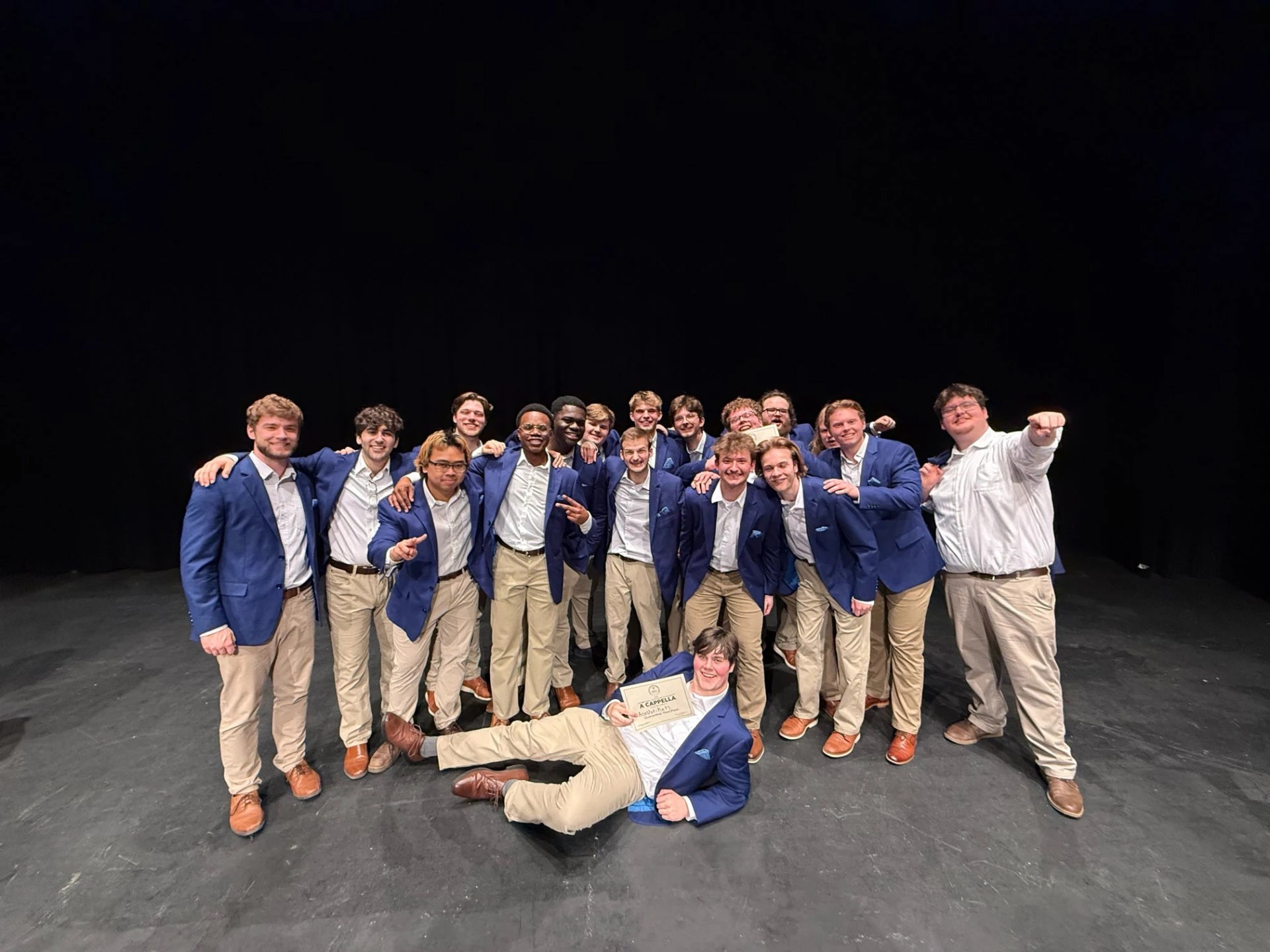The acoUstiKats posing onstage, with one member holding a certificate across the front.